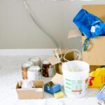 A cluttered room with renovation supplies including paint cans, boxes, and tools.